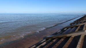 A coastal walkway with steps leading to the water, a clear sky, and distant landforms.