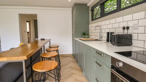 A modern kitchen with a wooden bar stool area, a built-in oven, and a window with a view of trees.
