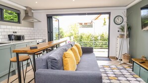 A modern kitchen with a grey sofa, wooden bar stools, and a patterned rug.