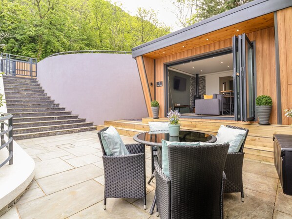 Eine moderne Außenpatio mit Korbmöbeln, einer Steintreppe und einem Holzdeck, das zu einer Glastür führt.
