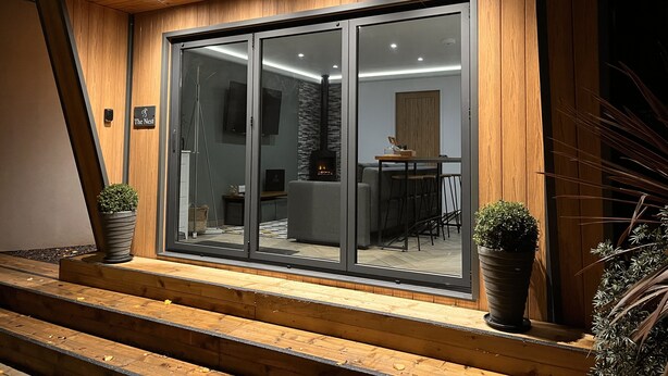 A modern building with a glass door entrance, a fireplace, and a dining area visible through the glass.
