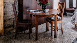 Un rincón de comedor rústico con una mesa redonda, dos sillas, un florero con flores y un libro.