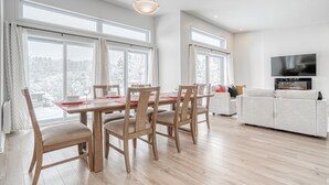 A modern living room with a dining area, large windows, a flat-screen TV, and a sofa. - Modern chalet B (Gatineau)
