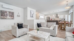 A modern living room with two grey sofas, a white coffee table, and a dining area with a wooden table and chairs. - Modern chalet B (Gatineau)