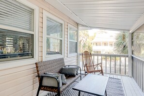 Relax on the covered porch with a woven bench, chair, and small table.