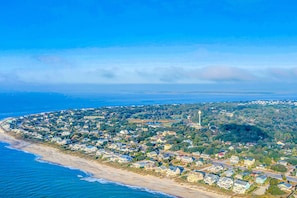 Stunning coastal homes line the beachfront, surrounded by lush greenery and a historic lighthouse in the distance.