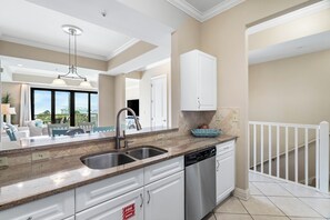 A modern kitchen with a double sink, stainless steel dishwasher, and white cabinetry. - Abacos 302 -Steps from the Beach, Beach View, close to restaurants on 30A (Santa Rosa Beach)