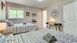 A bedroom with two beds, a desk, a chair, a window, and a door.