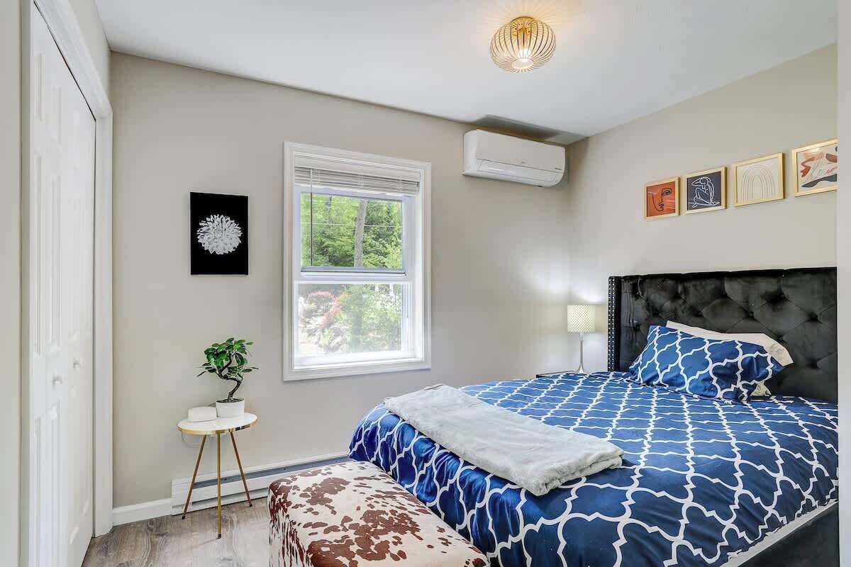 Une chambre avec un grand lit, une fenêtre, une petite table avec une plante et des œuvres d’art accrochées au mur.