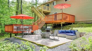 A wooden deck with outdoor furniture, a barbecue grill, and a red umbrella.