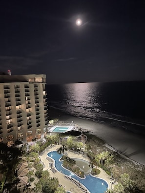 Un hôtel doté d’une piscine, offrant une vue sur la plage et une ambiance romantique sous la lumière de la lune.