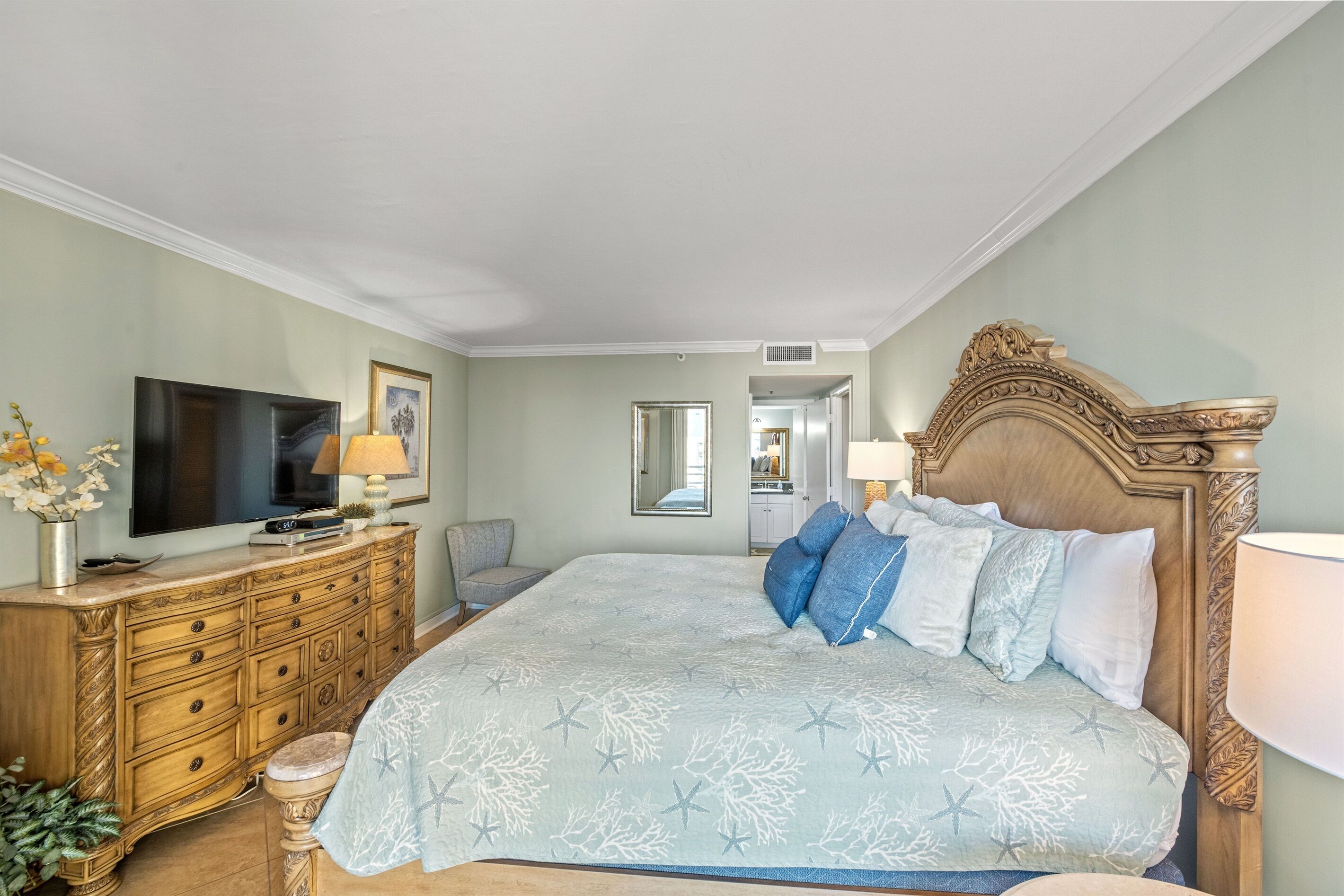 A bedroom with a large bed, a dresser, a TV, and a mirror.