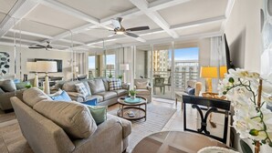A spacious living room with a high ceiling, ceiling fan, and large windows offering a city view. - N Hampton 1609 in Kingston, Oceanview, Pool, Beach (Myrtle Beach)
