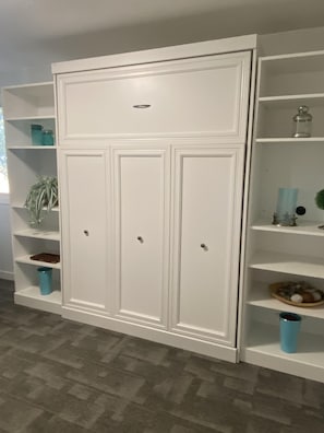 A white wardrobe with three doors and a small drawer, flanked by white shelving units with various items. - Country Farmhouse (between Lethbridge & Coaldale) (Lethbridge County)