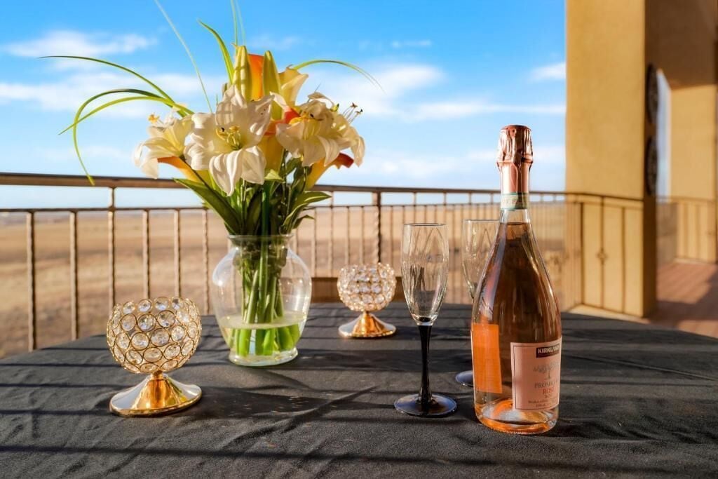 Una mesa dispuesta con una botella de vino, un jarrón de flores y dos copas de cristal en un balcón con vistas.