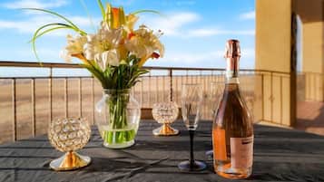 Una mesa dispuesta con una botella de vino, un jarrón de flores y dos copas de cristal en un balcón con vistas.