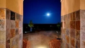 Vista nocturna de un pasillo con suelo de baldosas y paredes, que conduce a un cielo oscuro con una luna visible.