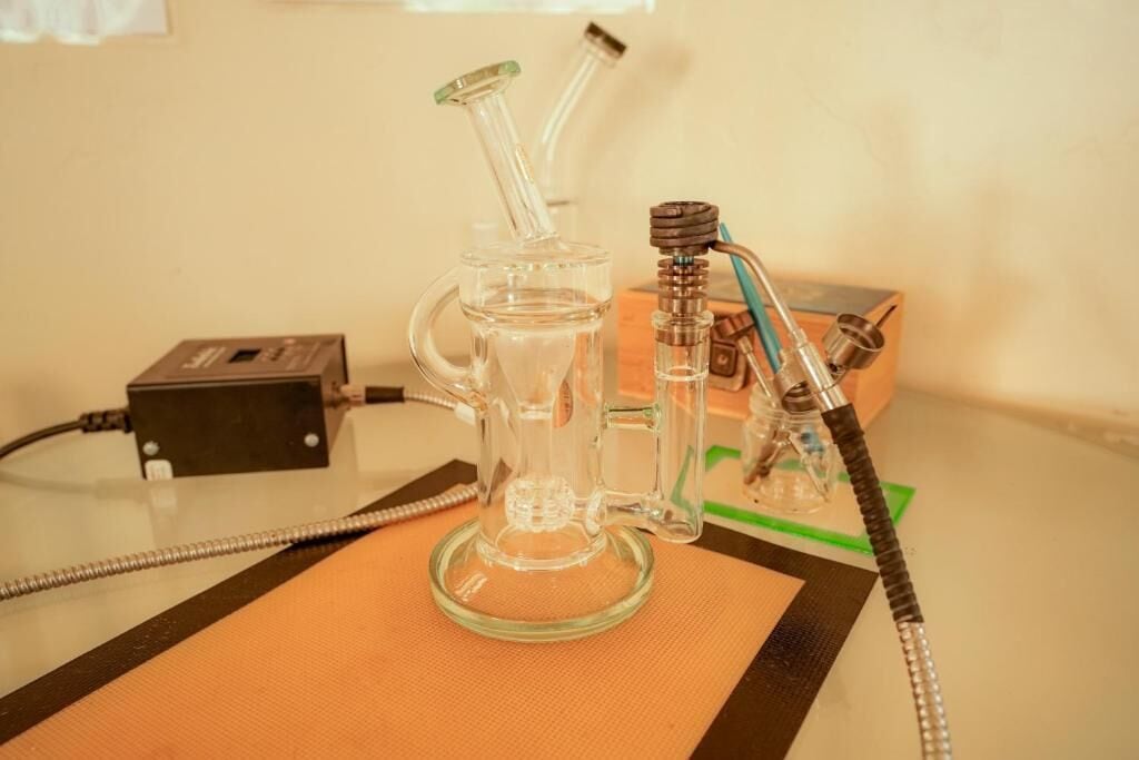 A glass bong on a table with a power adapter and a hookah pipe.