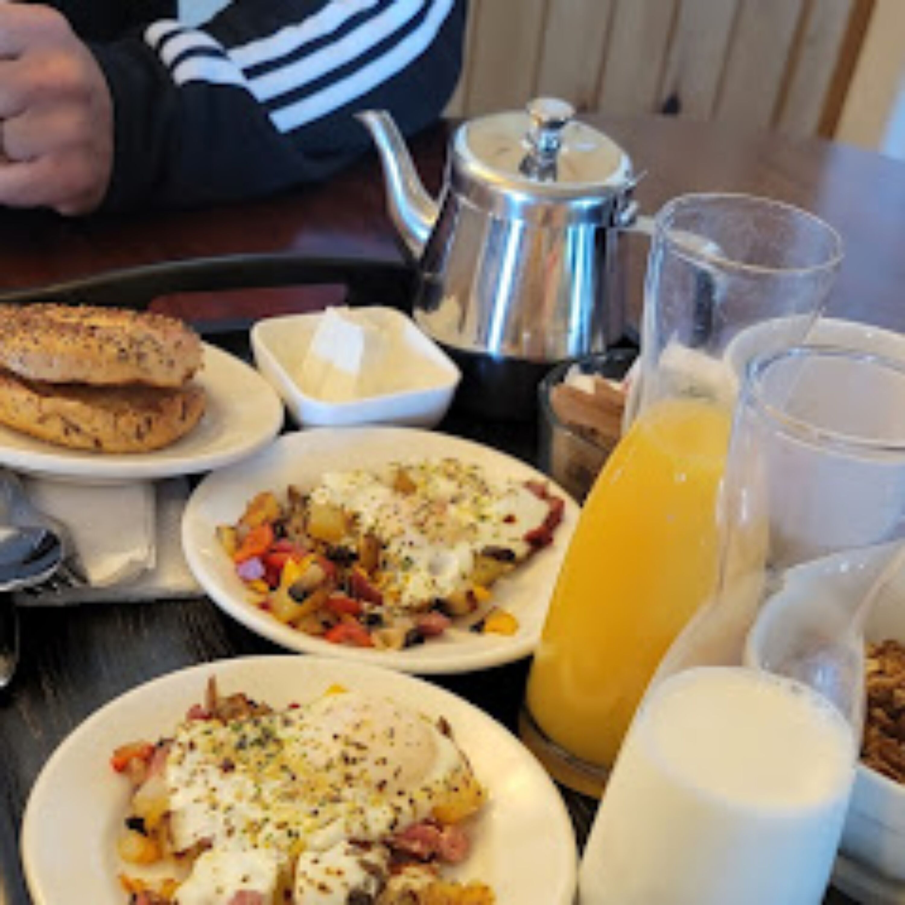Una mesa de desayuno con diversos platos, un calentador de té y un vaso de zumo de naranja.