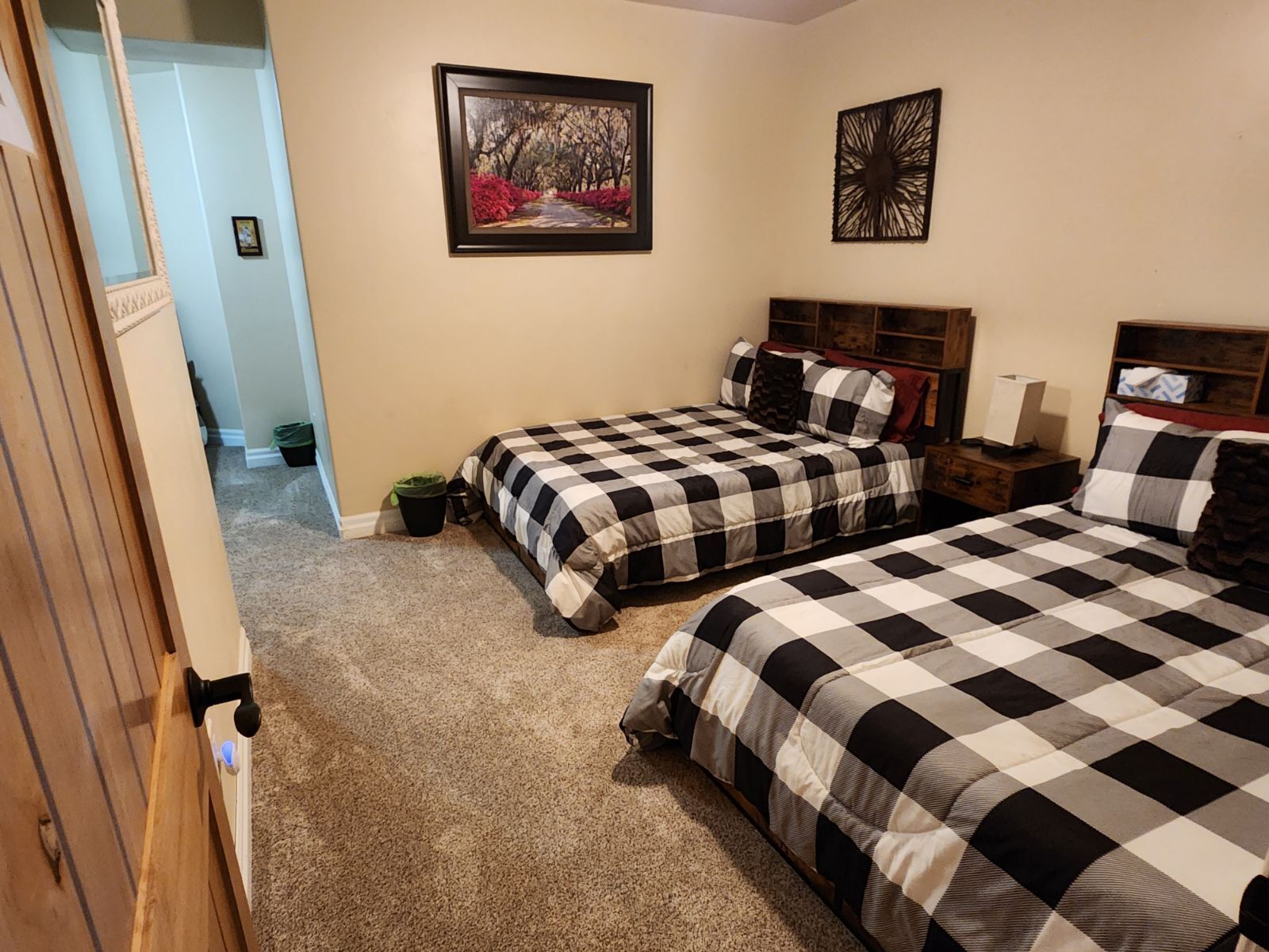 Une chambre avec deux lits, un tableau au mur et une petite poubelle.