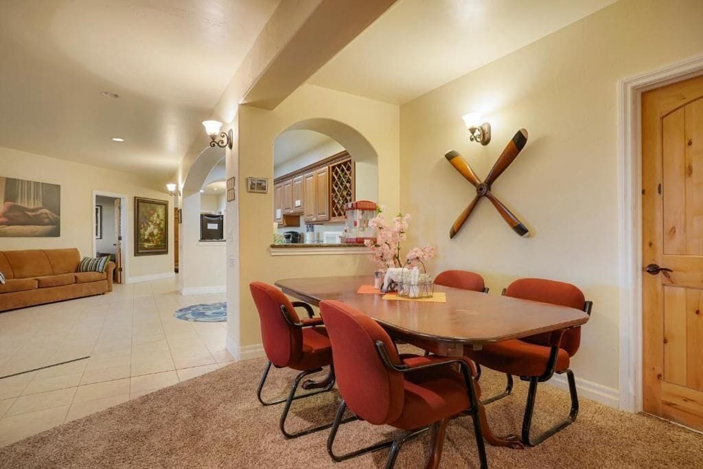 A dining area with a wooden table and red chairs, a kitchen in the background, and a wooden door.