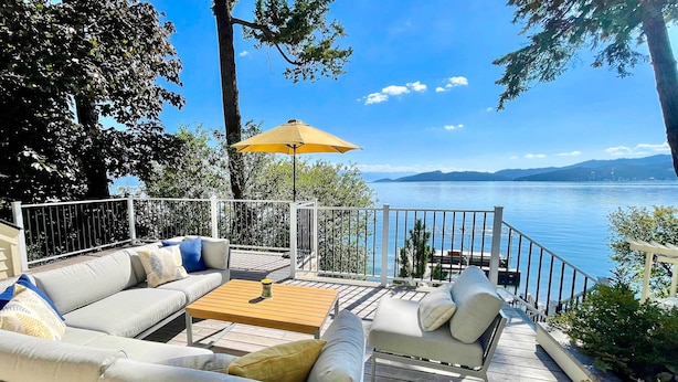 Una terrazza con divano, sedie e tavolo, con vista su un lago e montagne sullo sfondo.
