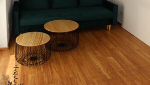 A modern living room with a dark green sofa, two round wooden tables, and a woven ceiling light fixture.