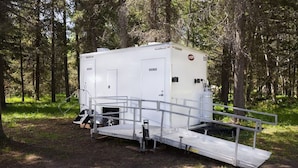 A portable shower unit with a ramp, set in a wooded area. - Yellowstone Family Tipi sleeps 7, w/ 1 king (Island Park)