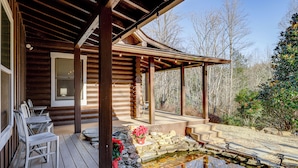 Une cabane en bois dotée d’un porche couvert, d’un escalier en pierre et d’un petit étang.