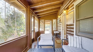 L’intérieur d’une cabane en rondins, avec un plafond en bois, un canapé, un fauteuil et une vue sur l’extérieur.
