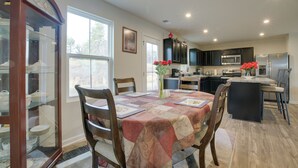A modern kitchen with dark cabinets, a central island, and a dining area with a table set for four. - 9 Mi to Duke University: Spacious Home w/ Yard! (Durham)
