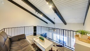 Ein modernes Wohnzimmer mit einem braunen Ledersofa, einem weißen Couchtisch mit Pflanze und einem schwarzen Geländer mit Blick auf einen Balkon.