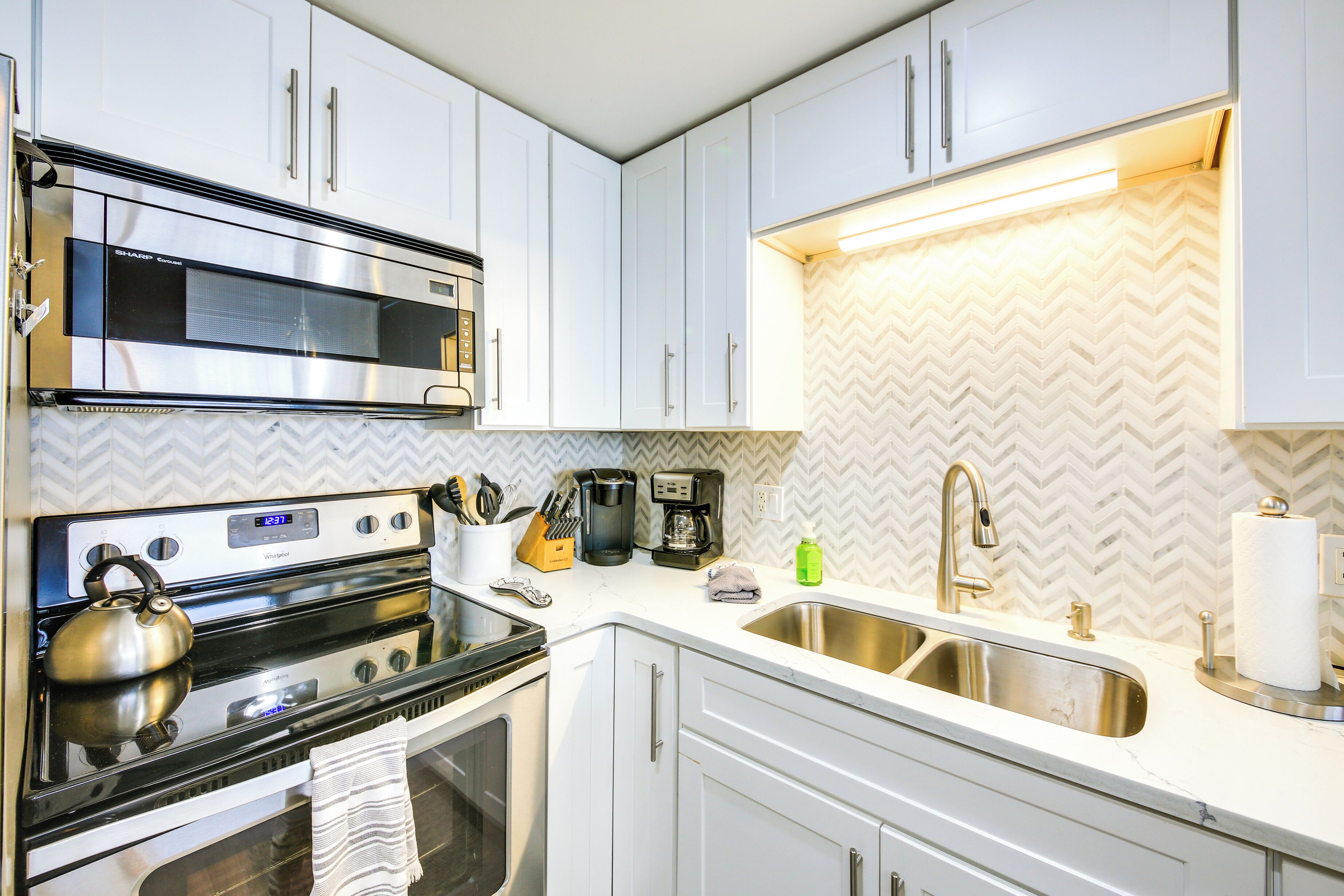 A modern kitchen with white cabinets, stainless steel appliances, and a herringbone patterned backsplash.