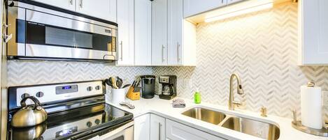A modern kitchen with white cabinets, stainless steel appliances, and a herringbone patterned backsplash.