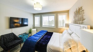 Ein modernes Hotelzimmer mit Bett, Fernseher, Stuhl und einem Fenster mit Jalousien.