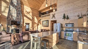 Un vaste espace de vie agrémenté d’une cheminée en pierre, d’un plafond en bois et d’une cuisine équipée d’appareils électroménagers modernes.