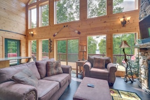 A spacious wooden cabin with a large living area featuring a sofa, armchairs, and a coffee table. Large windows provide views of the surrounding forest. - Paddle Ready: Hayward Lake View Retreat w/ BBQ (Hayward)