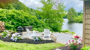 Ein Garten mit Grill, Adirondack-Stühlen und Seeblick.