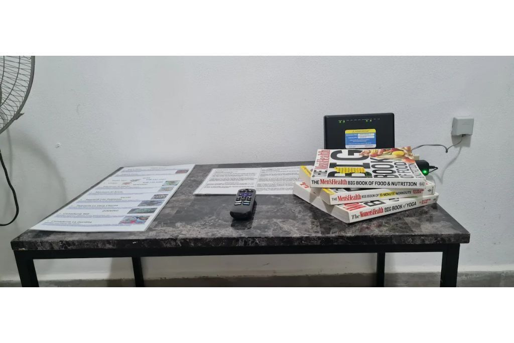 A table with a remote control, a computer, and several books.