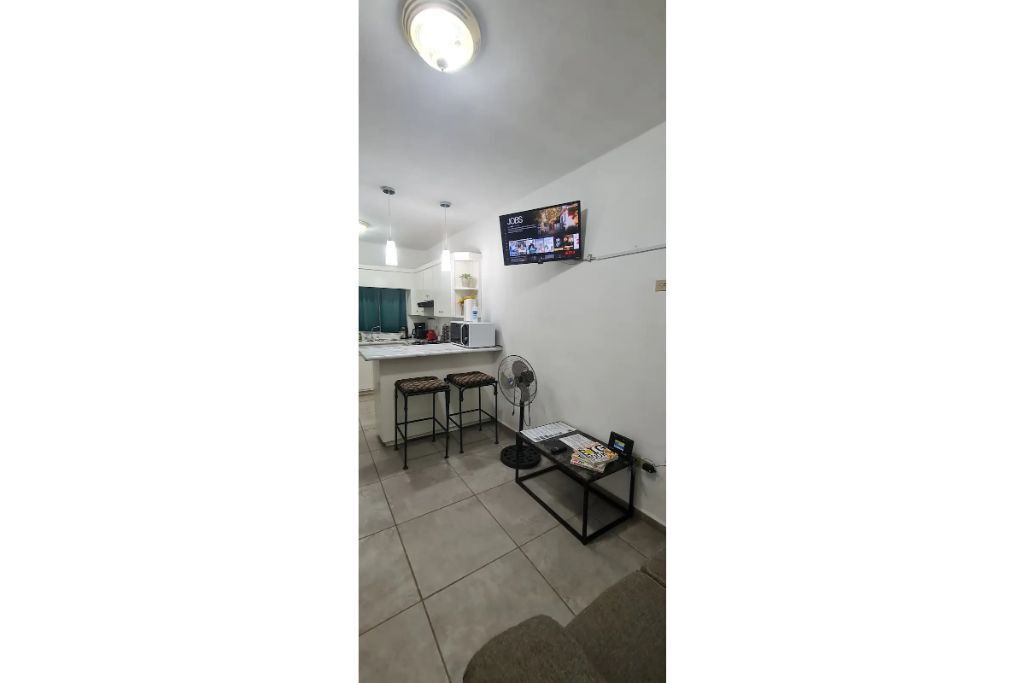 Un espace de vie compact comprenant un coin cuisine, une table à manger avec des chaises et un téléviseur fixé au mur.