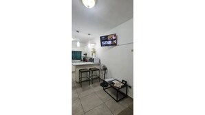 Ein kompakter Wohnbereich mit Küchenzeile, einem Esstisch mit Stühlen und einem an der Wand befestigten Fernseher.