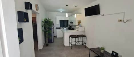Een moderne keuken met witte kasten, een zwart aanrecht en een ingebouwde magnetron. Er staan twee barkrukken bij een kleine tafel met een plant.