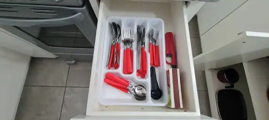 Un cassetto contenente utensili e un coltello con manico rosso.