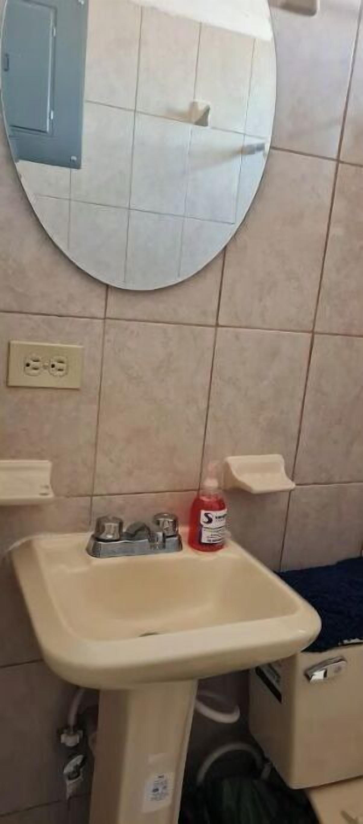 Un bagno con uno specchio rotondo, un lavandino e un piccolo ripiano.