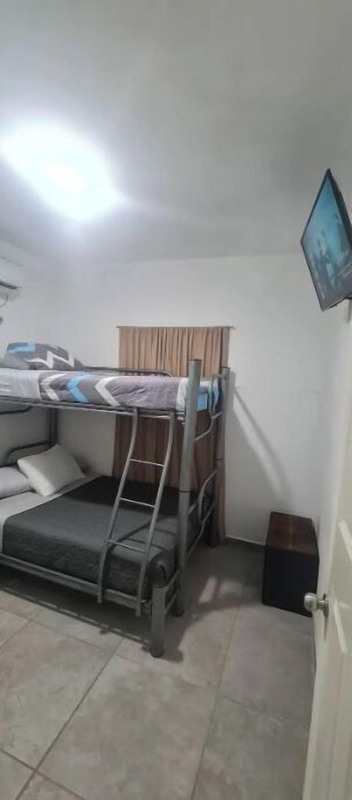 A small, compact room with bunk beds, a television mounted on the wall, and a door to the right.