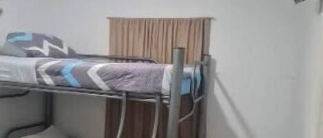 A small, compact room with bunk beds, a television mounted on the wall, and a door to the right.