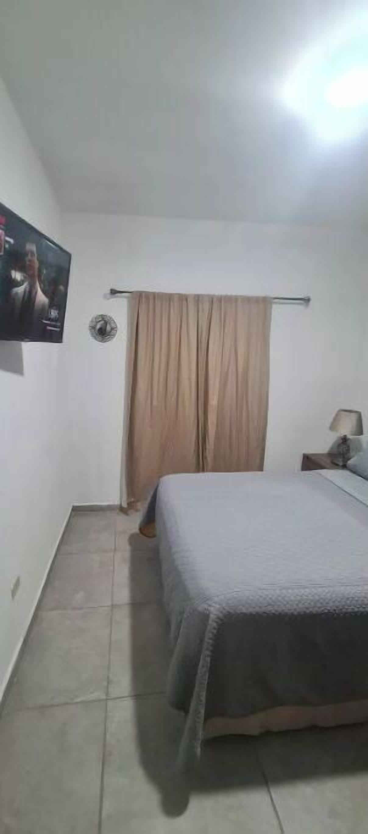 A bedroom with a bed, a TV mounted on the wall, a curtain, and a nightstand with a lamp.