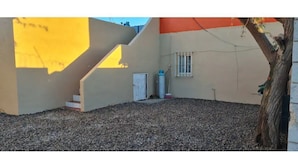 A building with a yellow and orange facade, a gravel driveway, and a tree. - Gated and secured Appartment 6 mins from the beach (Puerto Peñasco)