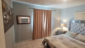 A bedroom with a bed, a nightstand, a wall-mounted air conditioner, and a window with curtains. - Gated and secured Appartment 6 mins from the beach (Puerto Peñasco)