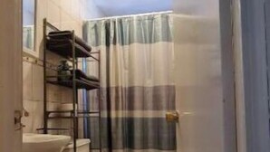 A narrow bathroom with a toilet, a sink, and a shower area. - Gated and secured Appartment 6 mins from the beach (Puerto Peñasco)